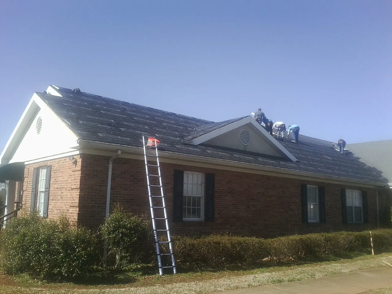 Crew tearing shingles off a brick ranch roof with a ladder set — Metal Roof Repair work by our crew in Rapidan