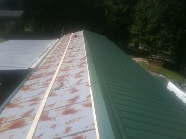 Old rusted panels beside newly installed green metal roofing — Wind Damage Roof Repair by Roofing Brothers in Rapidan